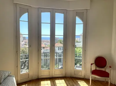 a bedroom with large windows with a red chair in front at SUPERBE 2 TERRASSES VUE MER in Cannes