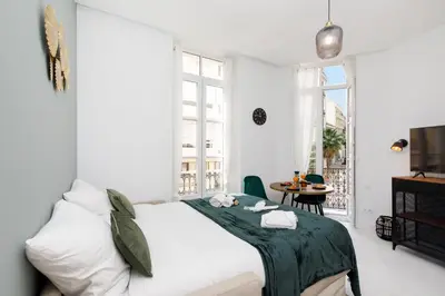 a white bedroom with a bed and a table at The Green Sun YourHostHelper in Cannes