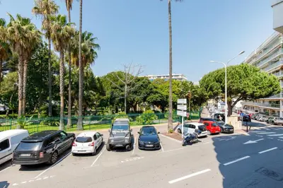 a parking lot with parked cars and palm trees at Les 3 Palmiers YourHostHelper in Cannes