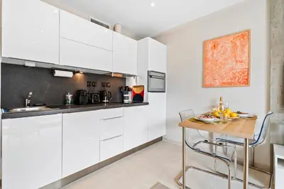 a kitchen with white cabinets and a wooden table at Downtown Cannes Modern 1-Br Apartment in Cannes
