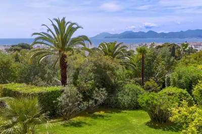a garden with palm trees and the ocean in the background at Cannes centre - Vue Mer, Piscine, Terrasse in Cannes