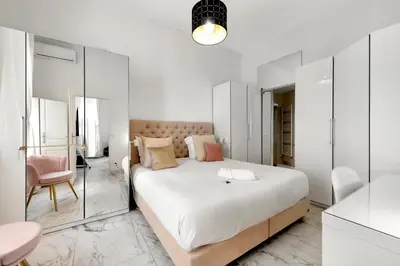 a bedroom with a large white bed and a pink chair at Le Borniol, splendid 3 bedrooms Appt, Cannes Center in Cannes