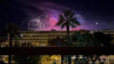 a fireworks display behind a building with a palm tree at Appartement cannes Croisette in Cannes