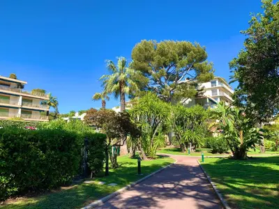 a path in a park with palm trees and a building at Appartement front de mer, 80M2 (3P), Piscine & Mer in Cannes