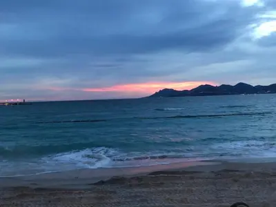 a sunset over the ocean with mountains in the distance at Boulevard de la croisette PALAIS MIRAMAR in Cannes