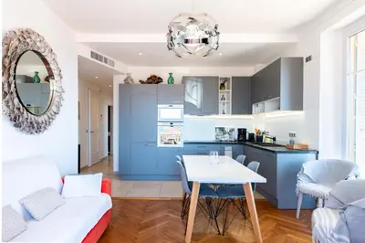 a kitchen and living room with blue cabinets and a table at LE SINATRA splendide vue mer panoramique et balcon, idéal pour des séjours de loisirs ou business in Cannes