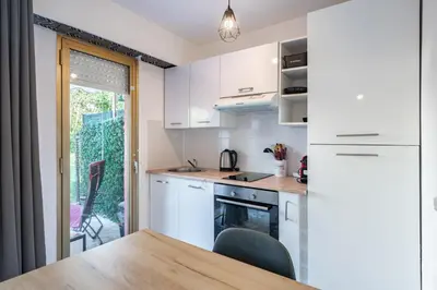 a kitchen with white cabinets and a table with chairs at Studio avec terrasse et jardin arboré - 5 min hypercentre Cannes in Cannes