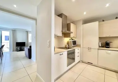 a kitchen with white cabinets and a living room at Appartement de deux chambres à coucher près de la Croisette à Cannes in Cannes