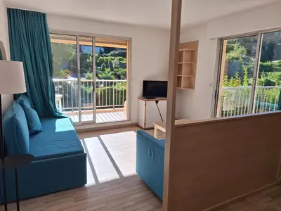 a living room with a blue couch and a window at 2 pièces climatisé dans résidence avec piscine in Cannes