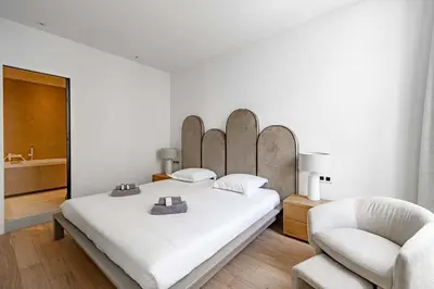 a white bedroom with a large bed and a chair at Superbe appartement 120m2 au coeur de Cannes in Cannes