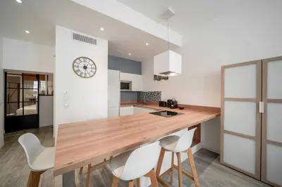 a kitchen with a wooden counter with white chairs at Appartement de charme proche Vieux Port et Palais in Cannes