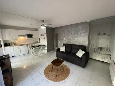 a living room with a black couch and a kitchen at Appartement proche mer in Cannes