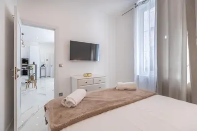 a white bedroom with a bed and a tv on the wall at LB Vacation Rentals I Renovated Apt Minutes from Beach - Palais - 30m2 Terrace in Cannes
