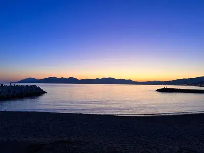 a sunset over a body of water with a beach at Les Arènes - Cannes centre, Charmant 2 pièces récemment rénové de 45 m2 avec sa terrasse de 10 m2 in Cannes