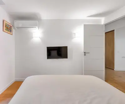 a white bedroom with a bed and a tv on the wall at LE MEYNADIER lumineux dans le centre historique, proche des plages et Palais in Cannes