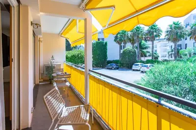 a yellow balcony with two benches and an umbrella at C9 - 2 BDR 10 min Palais Festivals & Sea - AC, Parking & Balcony in Cannes