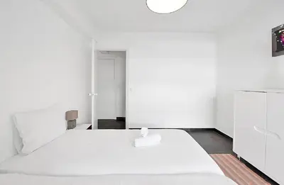 a white bedroom with a white bed and a light at LE VERSAILLES plaisir et confort en centre-ville, pour séjours en famille ou business in Cannes