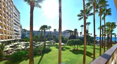 a view of a resort with palm trees and tables at Studio Cannes Grand Hôtel Cormoran avec Terrrasse in Cannes