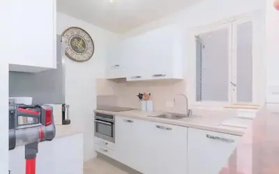 a kitchen with white cabinets and a clock on the wall at Le Concorde - Charmant appt avec terrasse in Cannes