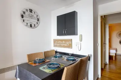 a dining room table with chairs and a clock on the wall at Appartement Wemyssia - Welkeys in Cannes