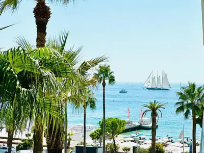 a view of a beach with palm trees and a sail boat at Grand Hotel - Studio Croisette in Cannes