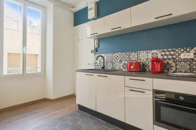 a kitchen with white cabinets and a blue wall at Studio Nid Doré - Welkeys in Cannes