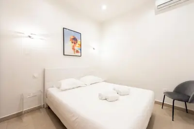a white bedroom with a bed and a chair at Renovated Apartment in the Heart of Cannes in Cannes