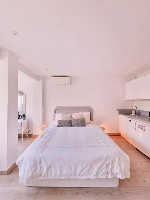 a white bedroom with a large bed and a kitchen at Studio Latour Maubourg in Cannes