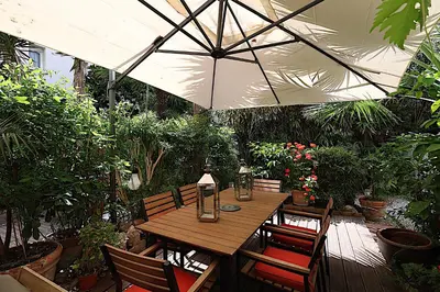 a wooden table with chairs and an umbrella in a garden at Appartement L'Etang Cannes Pointe Croisette in Cannes