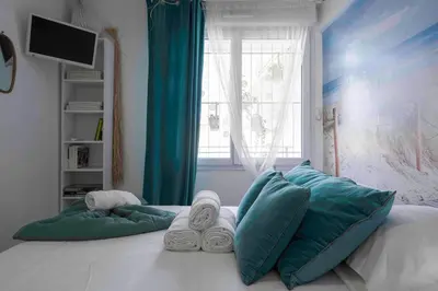 a bed with blue and white pillows and a window at Cannes Bliss - 12mn à pied du Palais, 5mn plages, clim, terrasse in Cannes