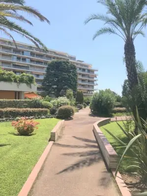 a walkway through a park with a building and palm trees at Studette Pointe Croisette - Axelle Loc'Appart in Cannes
