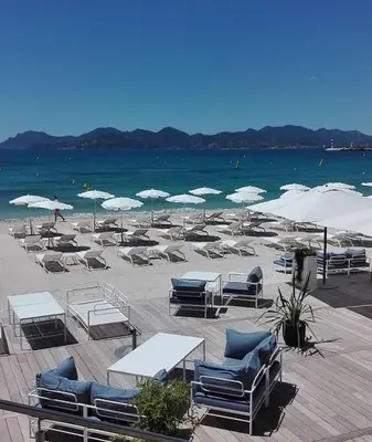 a sandy beach with chairs and tables and umbrellas at 2 pièces balcon 4 pers Meynadier Palais 1 minute by Olam Properties in Cannes