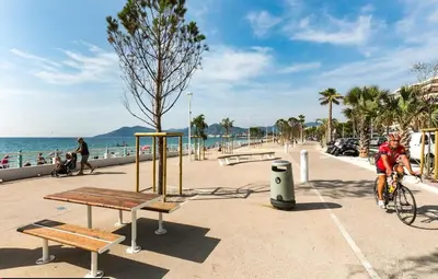 a person riding a bike on a sidewalk near the beach at Appartement Bord de Mer 4 pers / 2 Piscines in Cannes