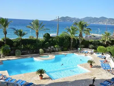 a swimming pool with palm trees and the ocean at Appartement Bord de Mer 4 pers / 2 Piscines in Cannes