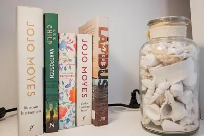 a shelf with books and a glass jar filled with shells at 