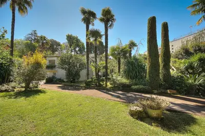 a garden with palm trees and a building at Le Bel - Jardin - Parking - VCA in Cannes