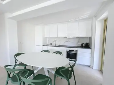 a white kitchen with a white table and green chairs at Modern 2 Bedroom in the Heart of Cannes in Cannes