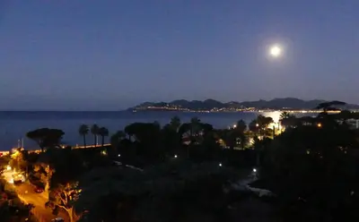 a full moon over the ocean at night at Apartment Montmorency in Cannes