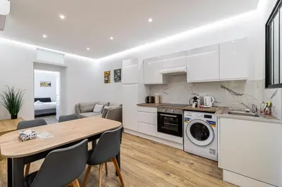 a kitchen and dining room with white cabinets and a wooden table at LE BAMBOO idéalement situé en centre-ville, pour familles ou petits groupes in Cannes