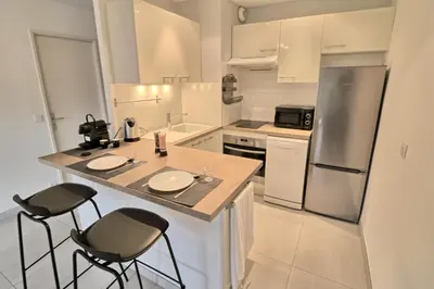 a kitchen with a counter with two chairs and a refrigerator at Appartement proche des Plages et du Palais in Cannes