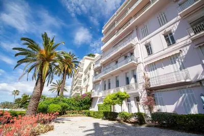 a large white building with a palm tree next to it at Brand New Central Cannes Apt 2 min walk to Palais in Cannes