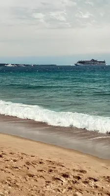 a beach with a cruise ship in the ocean at CANNES Appartement - terrasse, jardin prive, parking, piscine, climatisation in Cannes