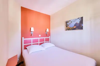 a bedroom with a white bed with an orange wall at Résidence Cannes Villa Francia - maeva Home - Appartement 2 pièces 4 personnes - Sélection MAE-2351 in Cannes