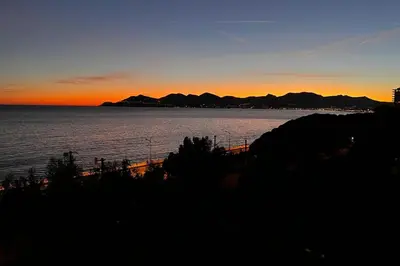 a sunset over the water with mountains in the background at 2-Br sea view private parking walk to beaches in Cannes