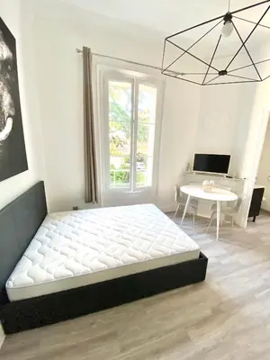 a white bedroom with a large bed and a table at Appartement Cosy in Le Cannet