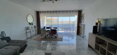 a living room with a couch and a table and a television at Spacieux 2 pièces terrasse et piscine in Cannes