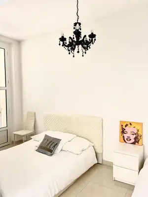 a white bedroom with a bed and a chandelier at Cannes plage 2 pièces Croisette centre ville in Cannes