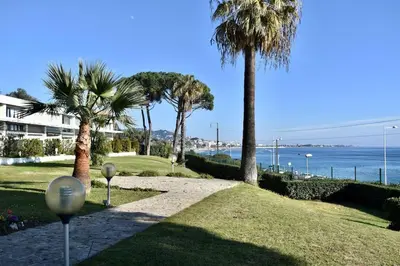 a walkway with palm trees and the ocean in the background at Studio bord de mer in Cannes