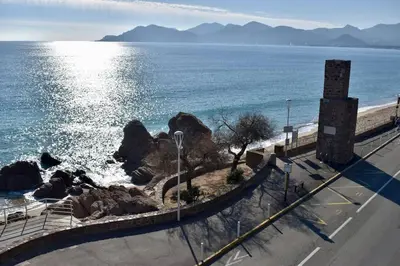 a road next to the ocean with mountains in the background at Studio bord de mer in Cannes