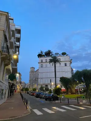 a city street with a large white building with a palm tree at Cocon Bohème Cannes Croisette-Palais-Plages 200m in Cannes